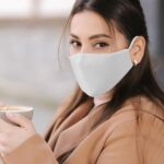 Woman wearing a light gray cloth mask while holding a coffee cup