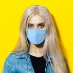 Woman wearing a light blue cotton mask against a yellow background