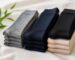 Stacks of folded knee-high socks in gray, navy, black and beige on a linen cloth beside green bamboo leaves