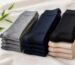 Stacks of folded knee-high socks in gray, navy, black and beige on a linen cloth beside green bamboo leaves